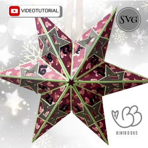 May include: A burgundy and grey star-shaped advent calendar with green trim. The star has cut-out numbers and a butterfly pattern. The image includes the text "VIDEOTUTORIAL" and the logo for "BINIBOOKS".