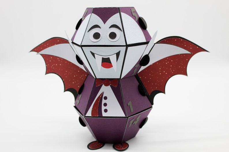 May include: A purple and white papercraft vampire with red wings and black eyes. The vampire has a bow tie and fangs. The numbers 1, 4, 5, 11, and 14 are visible on the sides of the vampire.