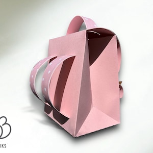 Puede incluir: Una bolsa de regalo de papel rosa con un patr&oacute;n de corazones blancos en las asas. La bolsa tiene un asa que se pliega sobre la parte superior.