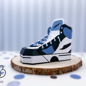 May include: A papercraft model of a blue, black and white high-top trainer. The trainer is sitting on a wooden base.