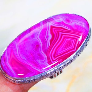 May include: A silver ring featuring a large oval pink agate gemstone. The agate displays a swirling pattern of pink and white.