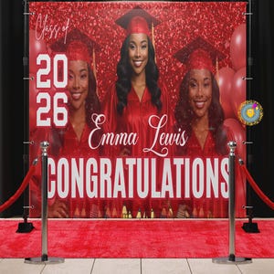 May include: A red graduation banner with the text "Class of 2026" and "Emma Lewis Congratulations". The banner features three images of a woman in a graduation cap and gown. A red carpet and stanchions are in front of the banner.