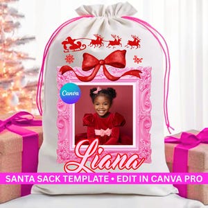 May include: White Santa sack featuring a red bow and a pink frame. The frame contains a photo of a child in a red dress. The sack has a drawstring closure and a design of Santa's sleigh and reindeer.
