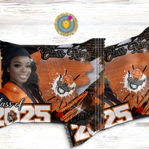 Może przedstawiać: Dwa opakowania cukierków z motywem ukończenia szkoły. Jedno opakowanie przedstawia uśmiechniętą absolwentkę w czapce i todze z napisem "Class of 2025". Opakowania mają pomarańczową, czarną i białą kolorystykę z grafiką pierścienia.