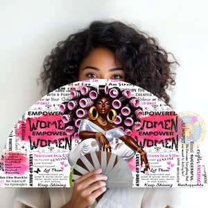 May include: A decorative fan featuring a black woman with curlers and gold jewelry. The fan has the words "Empower Women" in pink and white, along with inspirational phrases. The fan is held in front of a person's face.
