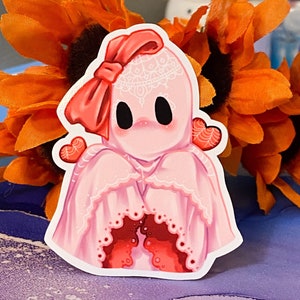 May include: A pink ghost wearing a white lace veil and a red bow. The ghost has red hearts on its arms and is holding its hands in front of its chest.