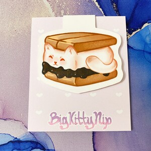 May include: A white cat shaped marshmallow is sandwiched between two brown graham crackers with a layer of chocolate in between. The image is on a light purple background with white hearts. The text "Big Kitty Nip" is at the bottom of the image.