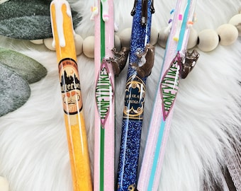 Op de afbeelding: Vier kleurrijke pennen met verschillende Harry Potter-themaontwerpen. De pennen zijn versierd met glitter, chocolade en snoep. De ontwerpen omvatten "Honeydukes", "Chocolate Frogs" en "Butterbeer".