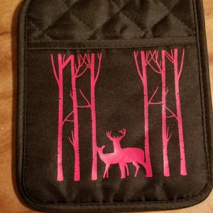 Puede incluir: Manopla de horno acolchada negra con una silueta de ciervo rosa en una escena de bosque.