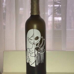 May include: A brown glass bottle with a white design of a woman and a skeleton on the front. The bottle is decorated with twine around the neck.