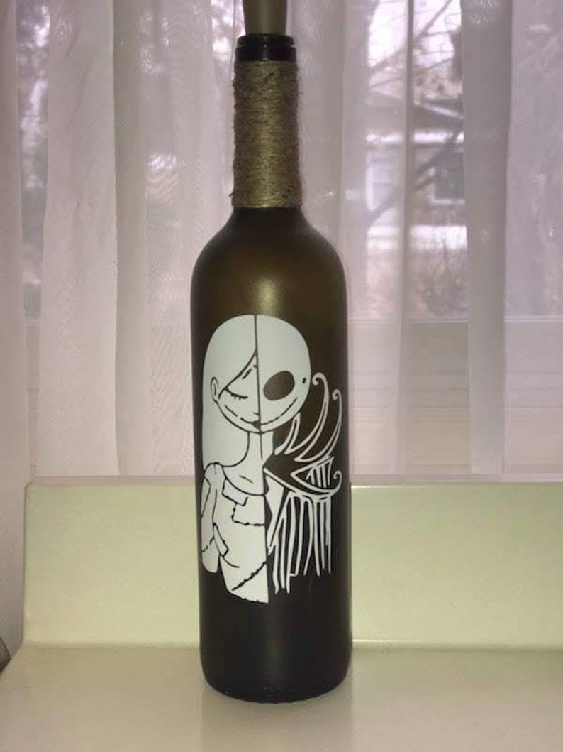 May include: A brown glass bottle with a white design of a woman and a skeleton on the front. The bottle is decorated with twine around the neck.