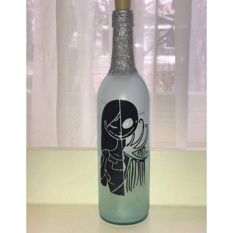 May include: A frosted glass bottle with a silver glitter top. The bottle has a black and white silhouette of Jack Skellington and Sally from the Nightmare Before Christmas.