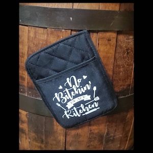 May include: Black quilted oven mitt with a white design that says "No Bitchin' In My Kitchen" with a ribbon and two spoons.