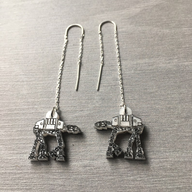 May include: A pair of silver dangle earrings featuring a detailed outline of an AT-AT walker from Star Wars.