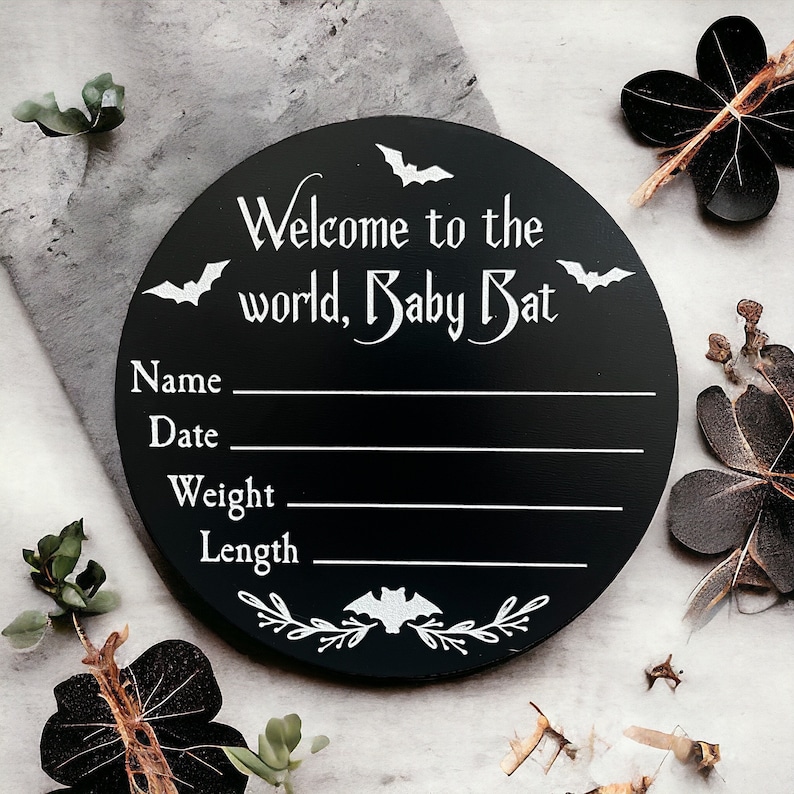 May include: Black round wooden sign with white bats and the text "Welcome to the world, Baby Bat". The sign has blank lines for name, date, weight, and length.