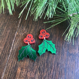 Pu&ograve; includere: Un paio di orecchini a forma di foglia di agrifoglio verde con bacche rosse a forma di teschio.
