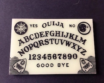 Könnte beinhalten: Ein weißes Ouija-Brett mit schwarzen Buchstaben und Symbolen. Das Brett enthält das Alphabet, die Zahlen 1-9 und 0, die Wörter "ja", "nein", "auf Wiedersehen" und Symbole für Sonne und Mond.