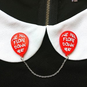 May include: Two red balloon pins with the text "We all float down here" attached to a silver chain. The pins are attached to a white collar.