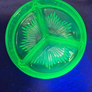 May include: A bright green, three-sectioned glass serving dish. The dish has a circular shape with a raised rim and a central divider creating three distinct compartments. The interior features a radial, sunburst-like pattern.