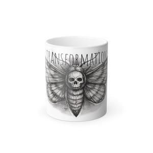 Puede incluir: Taza de cerámica blanca con una ilustración en blanco y negro de una polilla con cara de calavera. La palabra "TRANSFORMATION" está impresa encima de la polilla. La taza tiene un acabado brillante.
