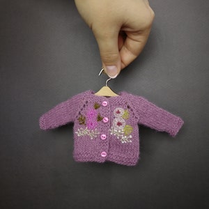May include: A purple knitted cardigan with embroidered flowers and buttons.
