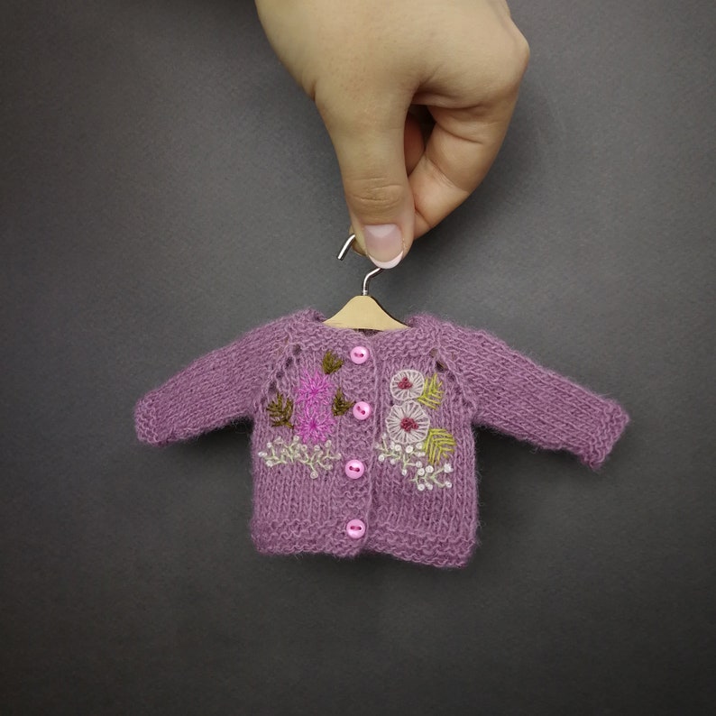 May include: A purple knitted cardigan with embroidered flowers and buttons.