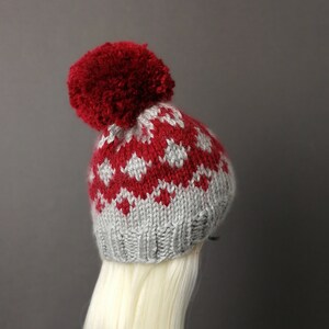 May include: A red and gray knitted hat with a pom-pom on top. The hat has a fair isle pattern.