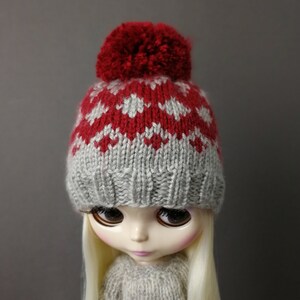 May include: A gray and red knitted hat with a red pom-pom on top. The hat is designed with a fair isle pattern.