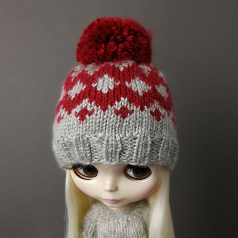 May include: A gray and red knitted hat with a red pom-pom on top. The hat is designed with a fair isle pattern.