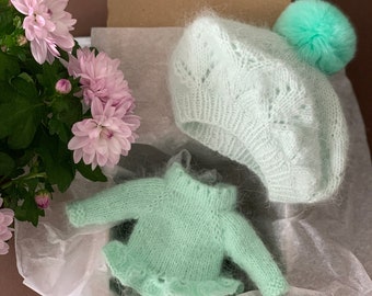 Può includere: Un maglione di lana verde chiaro per neonato con un orlo a balze e un berretto di lana verde chiaro abbinato con un pompon soffice.