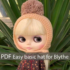 May include: A peach-colored knitted hat with a brown pom-pom on top. The hat is designed for a Blythe doll. The text "PDF Easy basic hat for Blythe" is at the bottom of the image.