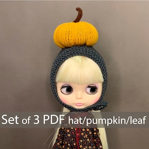 May include: Set of 3 PDF patterns for a knitted doll hat, pumpkin, and leaf. The hat is gray with a yellow pumpkin on top. The doll is wearing the hat and has blonde hair and blue eyes.
