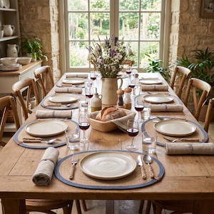 Large dinner table set with multiple blue striped oval jute placemats for a gathering with many guests.