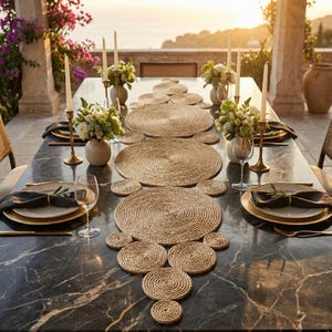 Marble terrace table at sunset laid with a jute circle runner, gold rimmed plates, white roses and tall taper candles overlooking the sea