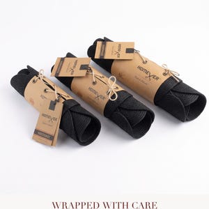 Black cotton rope item rolled and wrapped in kraft paper with cream twine and a kraft gift tag, with text reading Wrapped With Care, every order ships tied like this, ready to gift.
