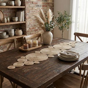 Dark farmhouse table with a jute circle runner, a large ceramic vase of eucalyptus and pampas, candles on a wooden tray and open shelving of pottery behind