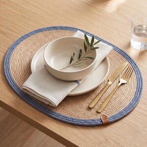 Close table setting on a denim blue striped jute placemat with plate, cutlery and linen napkin.