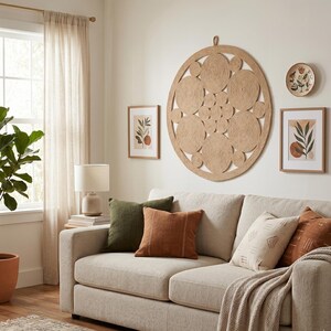 Round jute wall hanging in a living room above a cream sofa with olive and rust cushions, flanked by small botanical prints and a fiddle leaf fig
