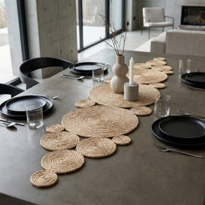 Modern concrete dining table with a jute disc runner, matte black plates, clear glasses and a pale sculptural vase against floor to ceiling windows