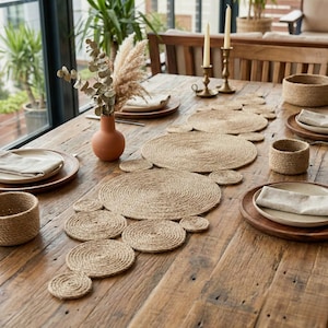 Reclaimed wood table beside tall windows with a jute disc runner, a terracotta vase of eucalyptus, brass candlesticks and woven napkin rings
