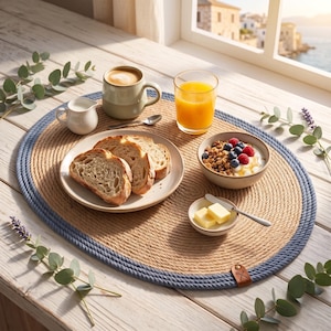 Nautical blue jute placemats styled with plates, mugs and greenery on a natural wood breakfast table.
