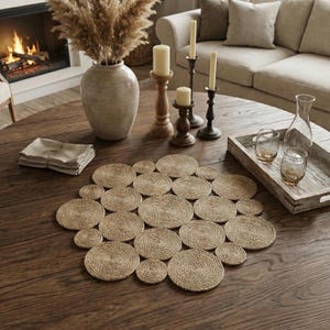 Puede incluir: Una mesa redonda de madera oscura está adornada con un mantel individual de yute tejido compuesto por múltiples posavasos circulares. La mesa incluye velas en candelabros, un jarrón con plantas secas y una bandeja de madera con vasos y una jarra.