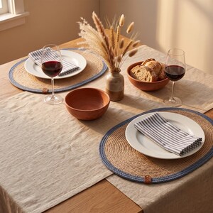 Denim blue oval jute placemat on a rustic table styled with dried pampas and dark stoneware plates.