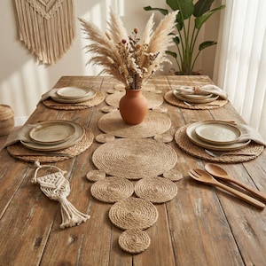 Overhead view of a farmhouse table with a jute coil runner, a terracotta vase of dried flowers, four woven placemats and stoneware plates