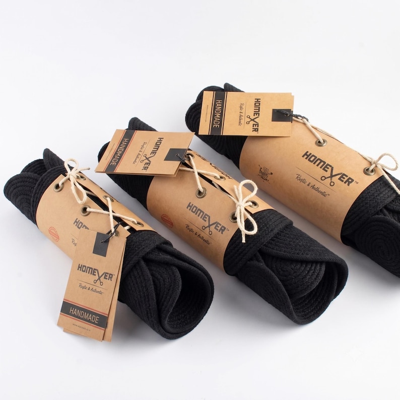 Homever packaging. Three black cotton rope runners rolled and wrapped in kraft paper sleeves with a Homever tag and a cotton tie, ready to gift. Every order arrives rolled, never folded.
