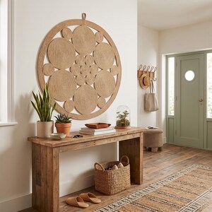Large jute wall hanging in a hallway above a reclaimed wood console, with snake plants, a glass cloche, a woven basket of shoes and a sage green front door