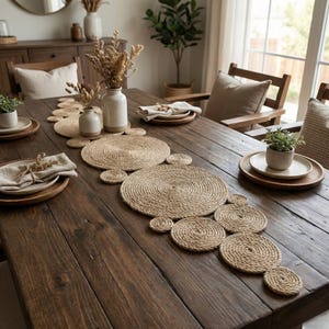 Dark wood farmhouse table with a jute circle runner down the centre, cream vases of dried grasses, a small potted plant and linen napkins on wooden chargers