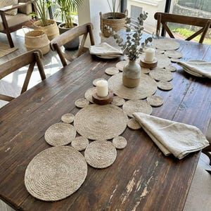 Könnte beinhalten: Ein rustikaler Holztisch ist mit einem Tischläufer aus Naturjute und passenden Platzsets gedeckt. Der Tisch ist mit Kerzen, einer Vase mit Trockenblumen und Leinen-Servietten dekoriert.