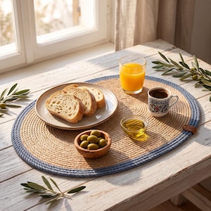 Denim blue striped jute placemats on a coastal table with sea view, styled with white plates and napkins.