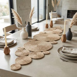 Pale concrete table with a jute coil runner, faceted wood candle holders, matte vases of pampas grass and simple grey plates